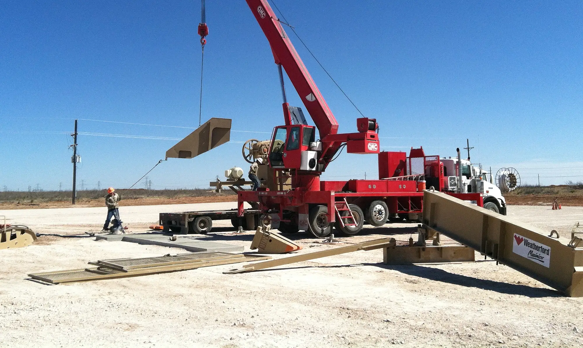 Red QMC crane lifting materials on an active construction site, illustrating the hands-on performance and reliability behind QMC Cranes.