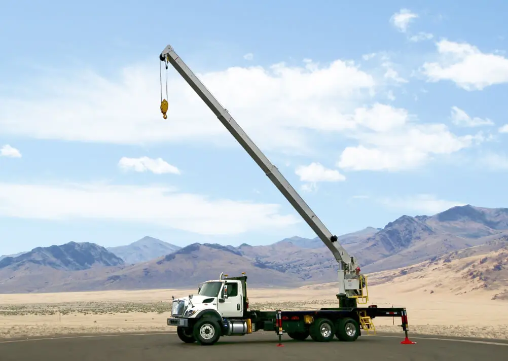 White QMC boom truck crane with fully extended boom positioned in a remote desert landscape, demonstrating boom truck cranes built for reach, power, and stability.