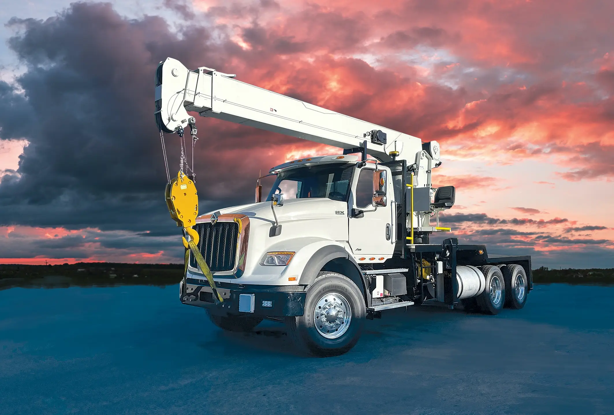 White QMC boom truck crane positioned under a dramatic sunset sky, representing legacy boom truck cranes built with enduring strength and reliability.