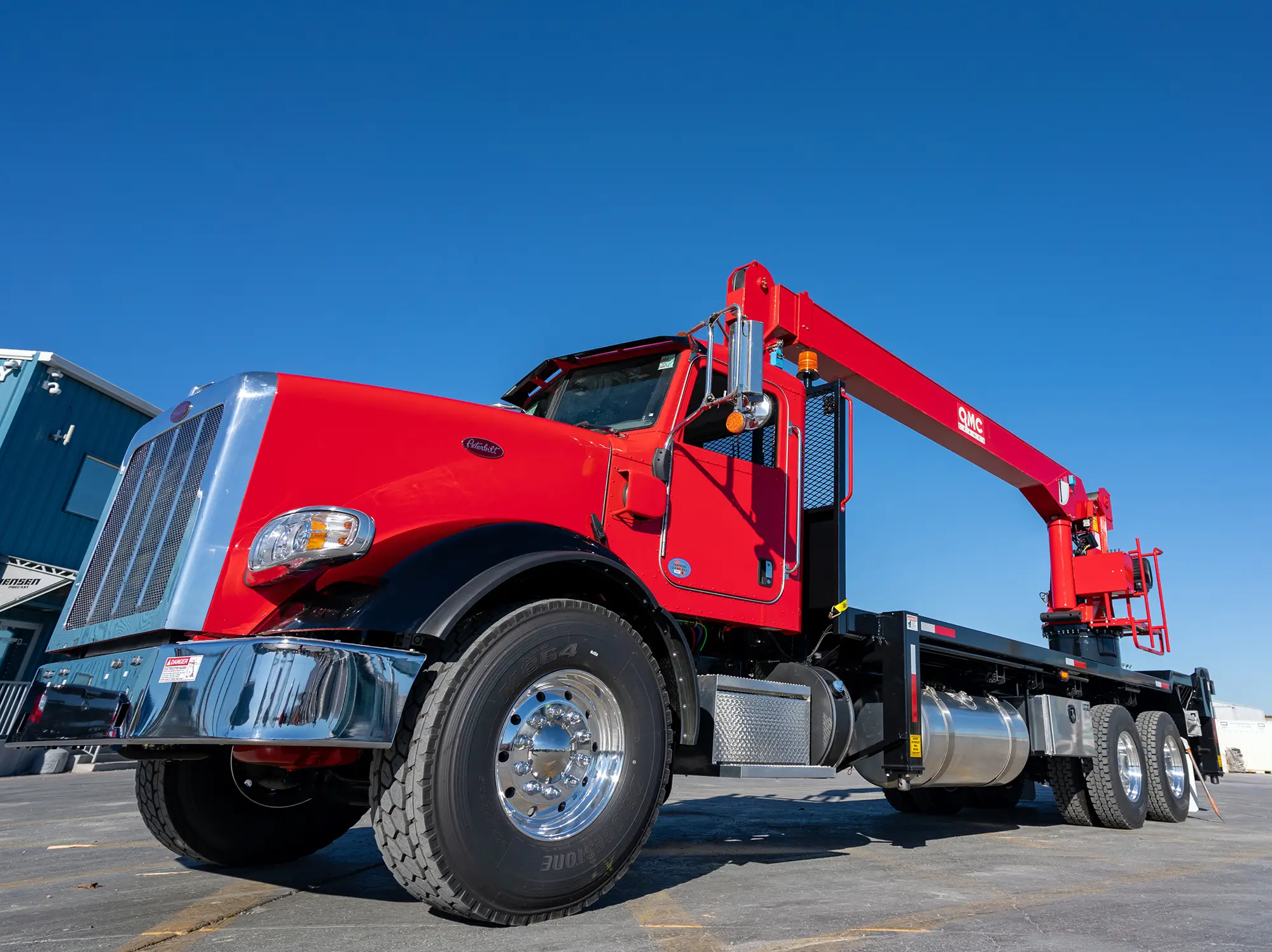 Red QMC boom truck crane parked on job site with extended boom arm, representing durable and custom-engineered boom truck crane models.