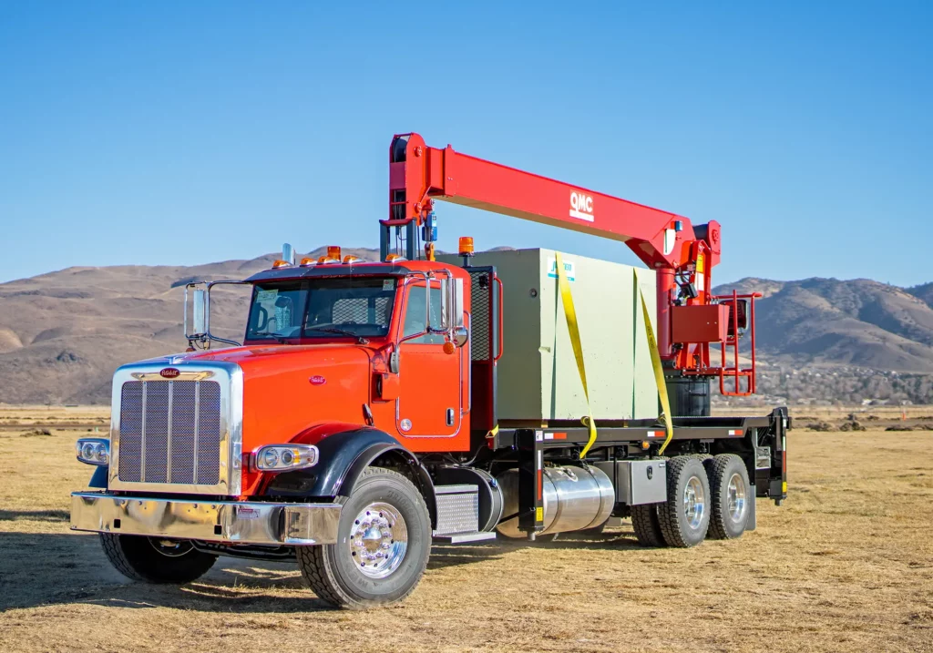 Red QMC rear-mounted boom truck crane positioned in an open field, representing high-capacity rear mount boom truck cranes designed for heavy lifting in rugged environments.