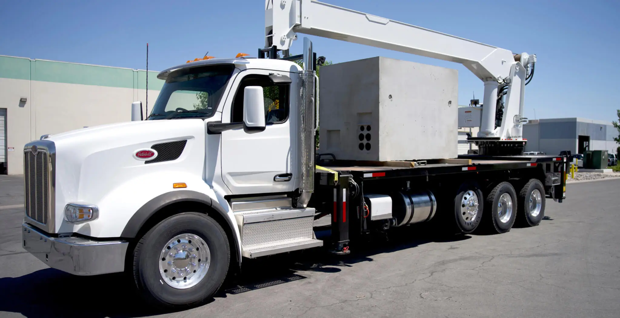 White QMC 5034R boom truck crane with rear-mounted 34' boom lifting a concrete load, showcasing high-lift boom truck cranes with four axles and heavy payload capacity.