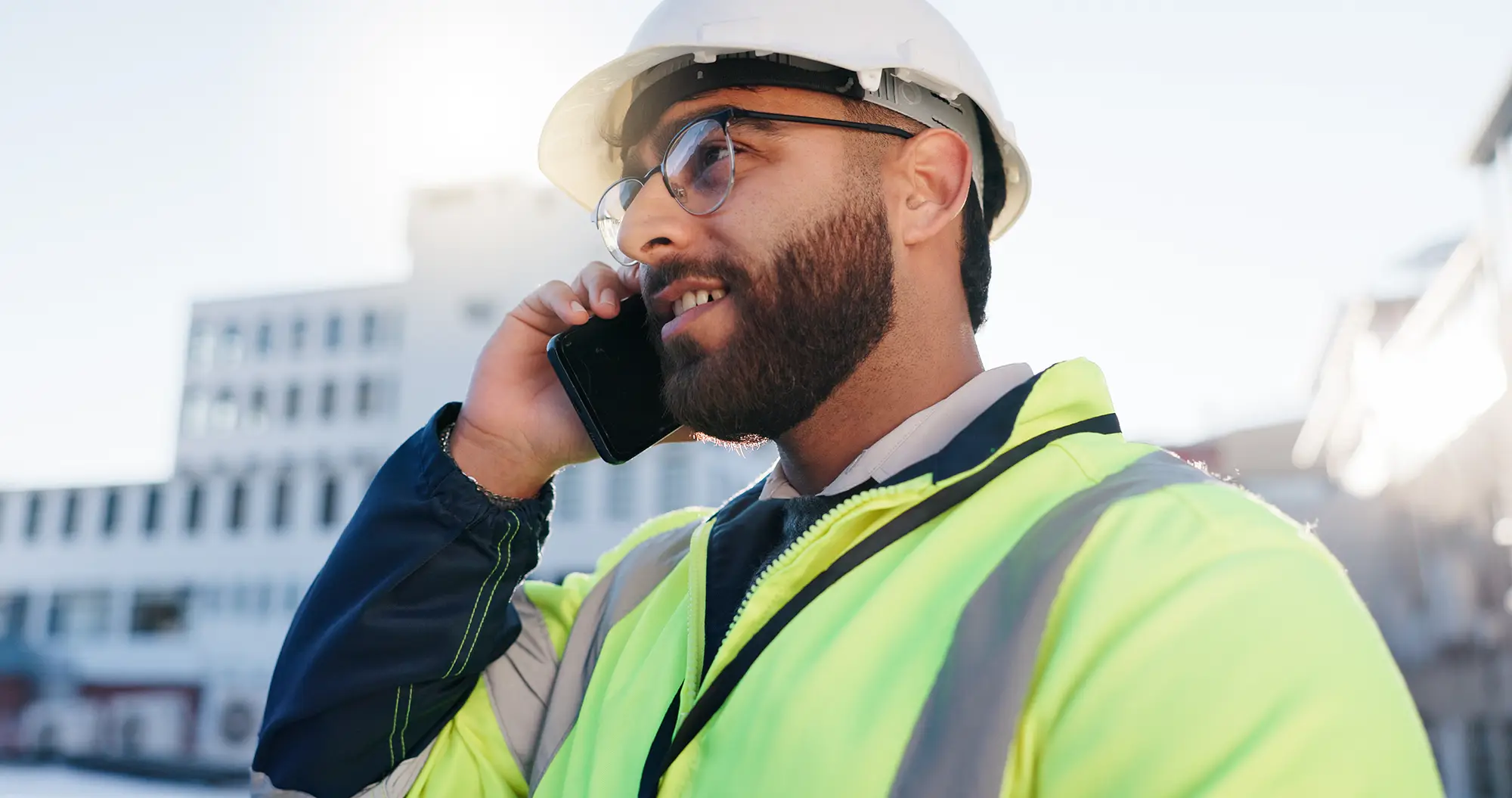 Construction worker in safety gear speaking on the phone at a job site, representing access to crane resources and expert support in the field.